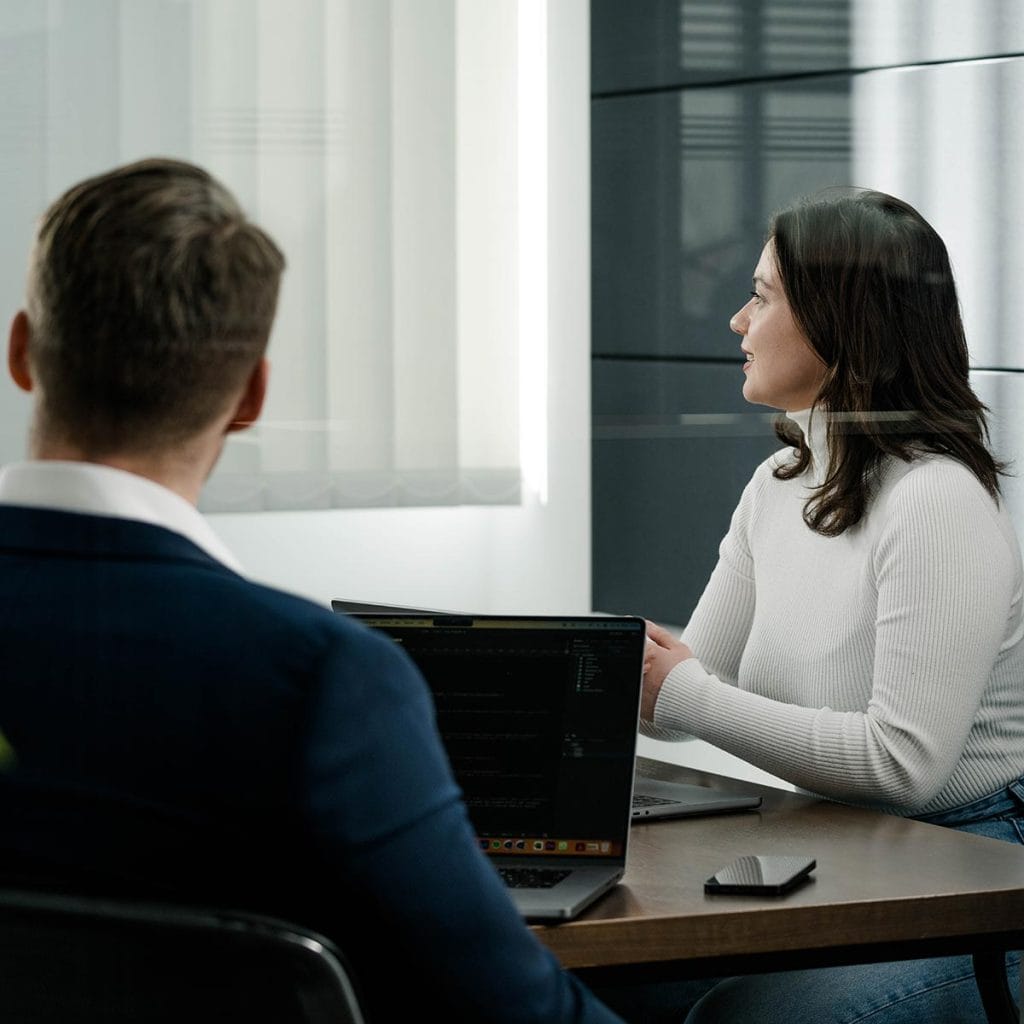 Ein angeschnittener Mann im Anzug und eine Frau sitzen in einem Meetingraum und betrachten gemeinsam eine Präsentation. Die Szene stammt aus einem authentischen Fotoshooting mit Dinape-Mitarbeitern, das im Rahmen der Content-Produktion durchgeführt wurde, um den professionellen und nahbaren Auftritt des Unternehmens zu unterstreichen.